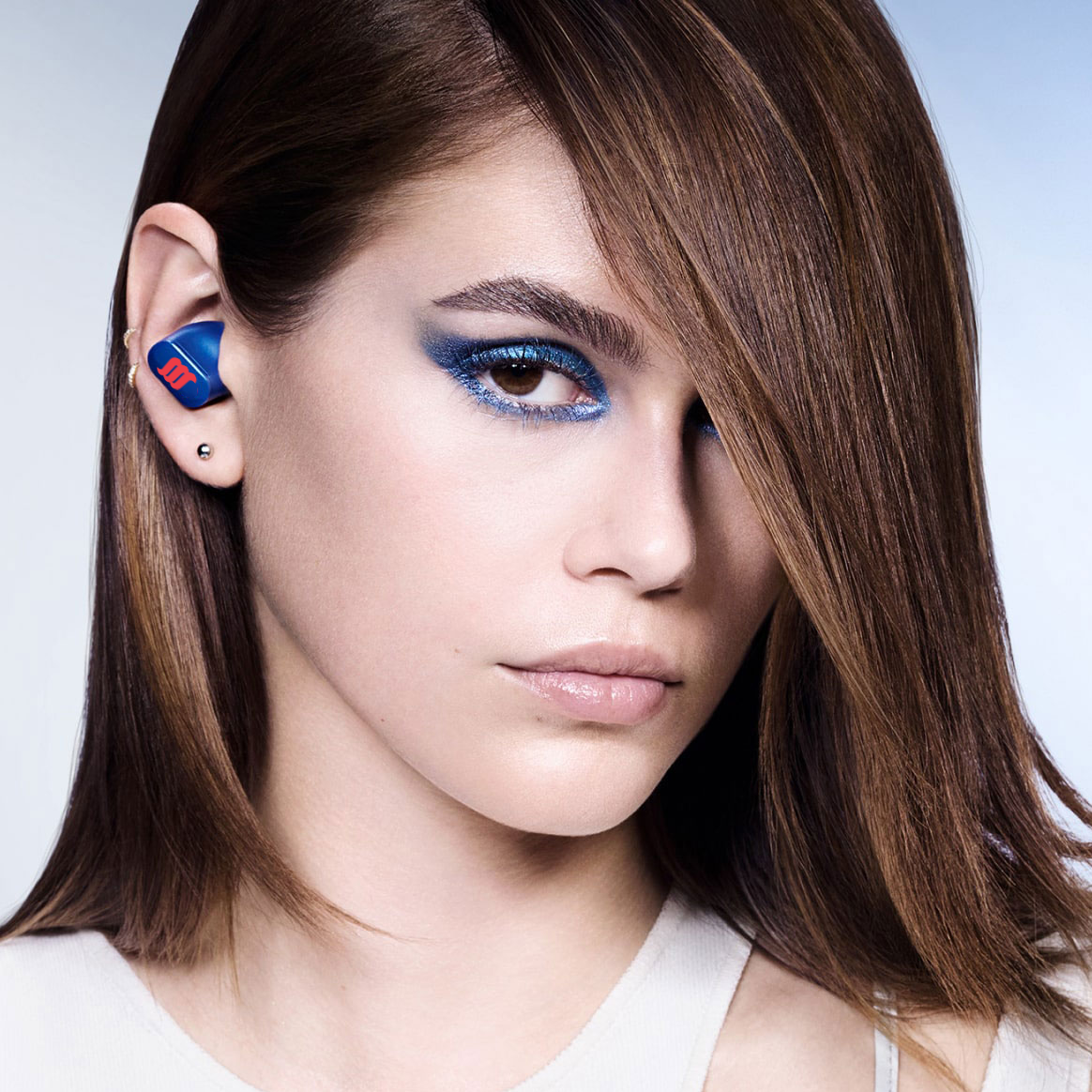 Caucasian female model wearing blue earbuds.